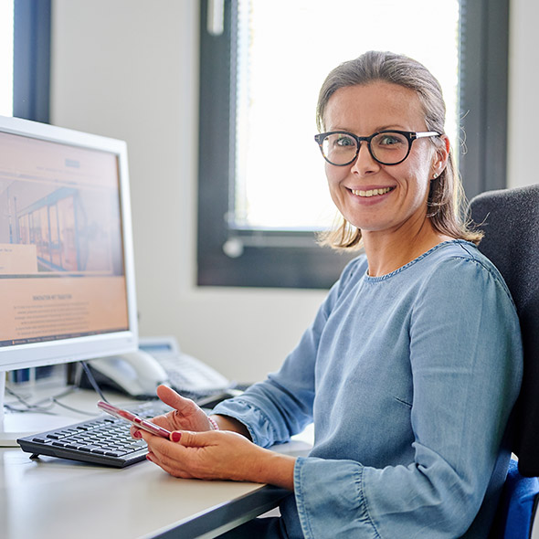 A woman in glasses working at a desk with a computer in front of her A woman in glasses working at a desk with a computer in front of her