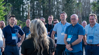A diverse group of individuals standing togther and listening to a lady